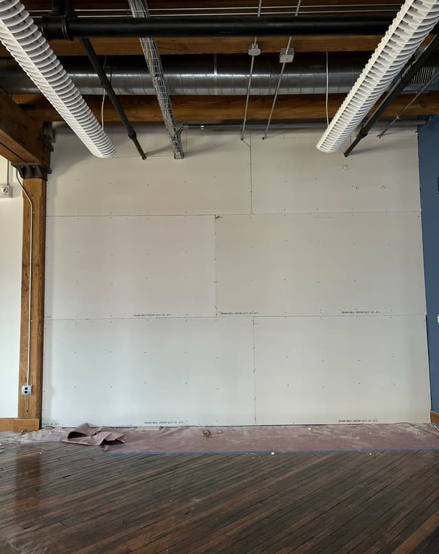 an empty room with a wood floor and exposed pipes